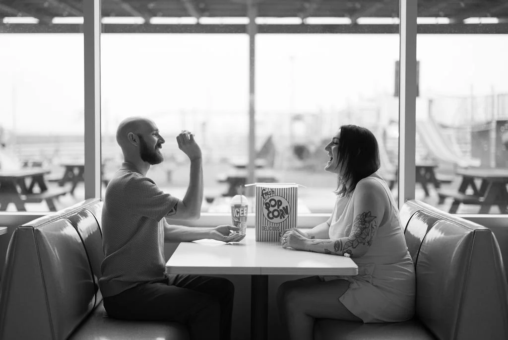 Couple tossing popcorn into each other's mouths across the booth at the Stars and Stripes Drive In diner