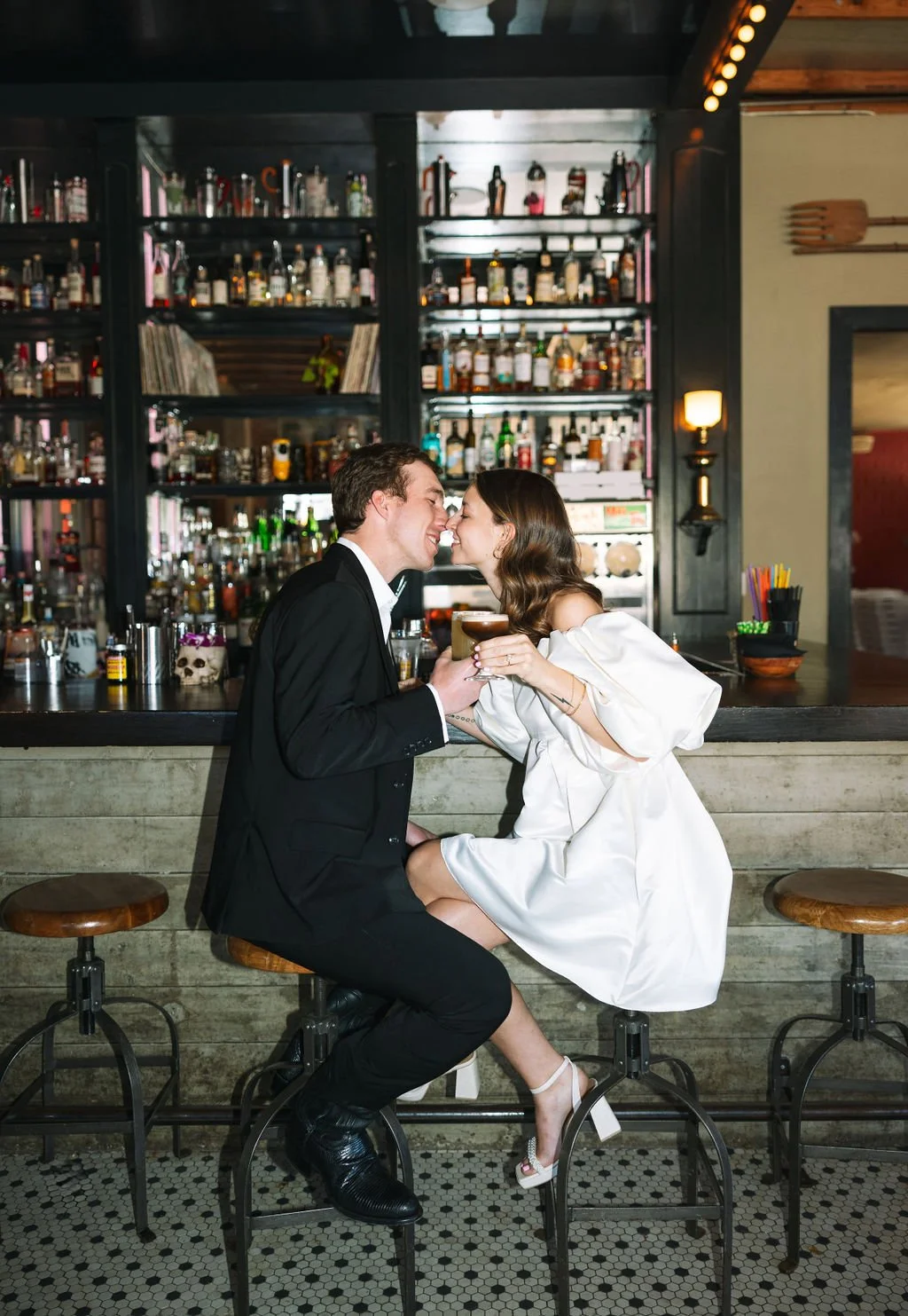 Couple sitting at bar stools kissing during Barbaro San Antonio engagement photos.