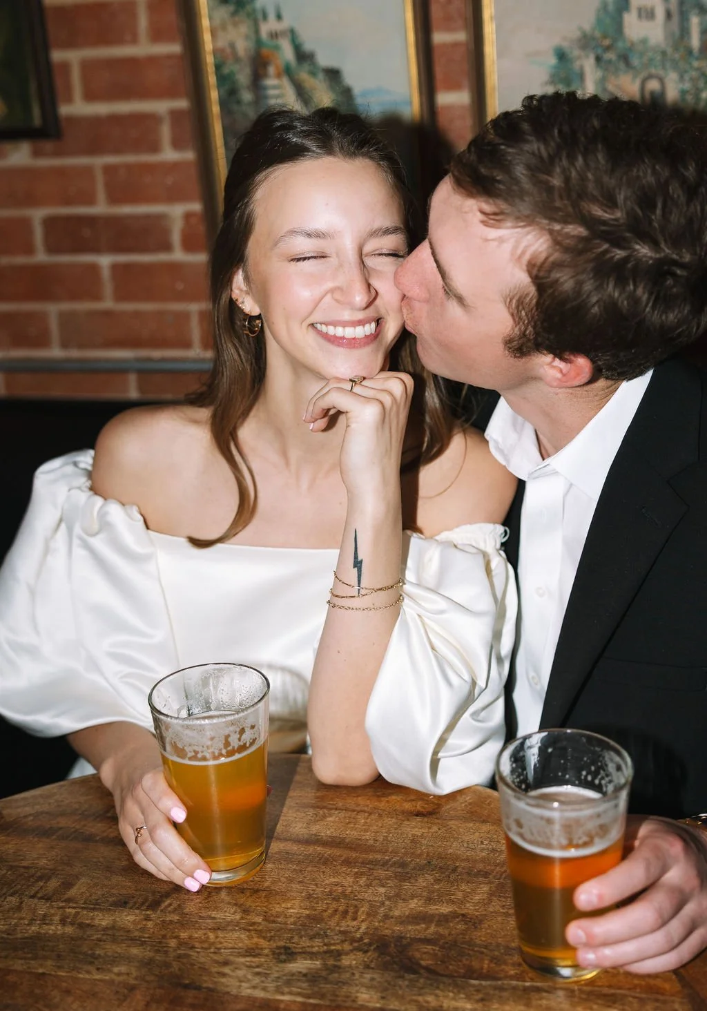 Couple kissing and smiling while enjoying pizza and beers at Barbaro restaurant during San Antonio engagement photos.