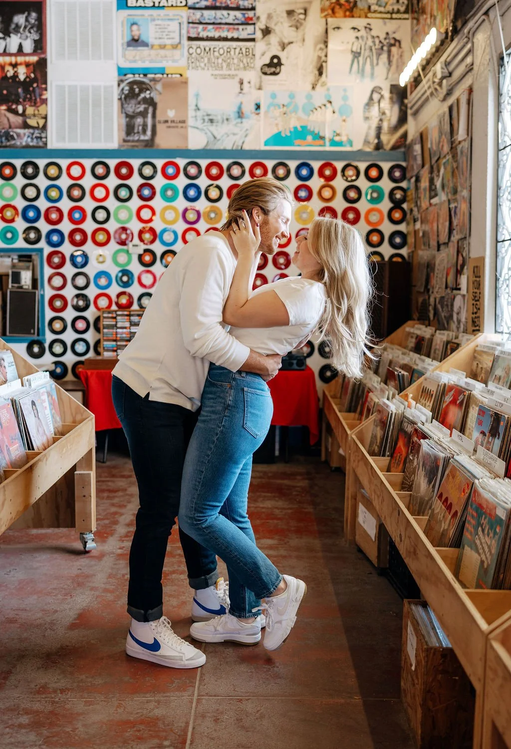 Couple kissing between record aisles inside Friends of Sound during San Antonio engagement photos.