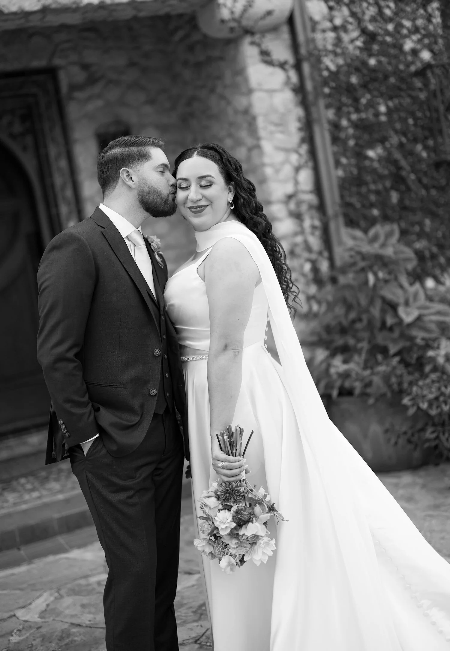 A Texas bride and groom stand lovingly together as the groom kisses the bride's cheek.