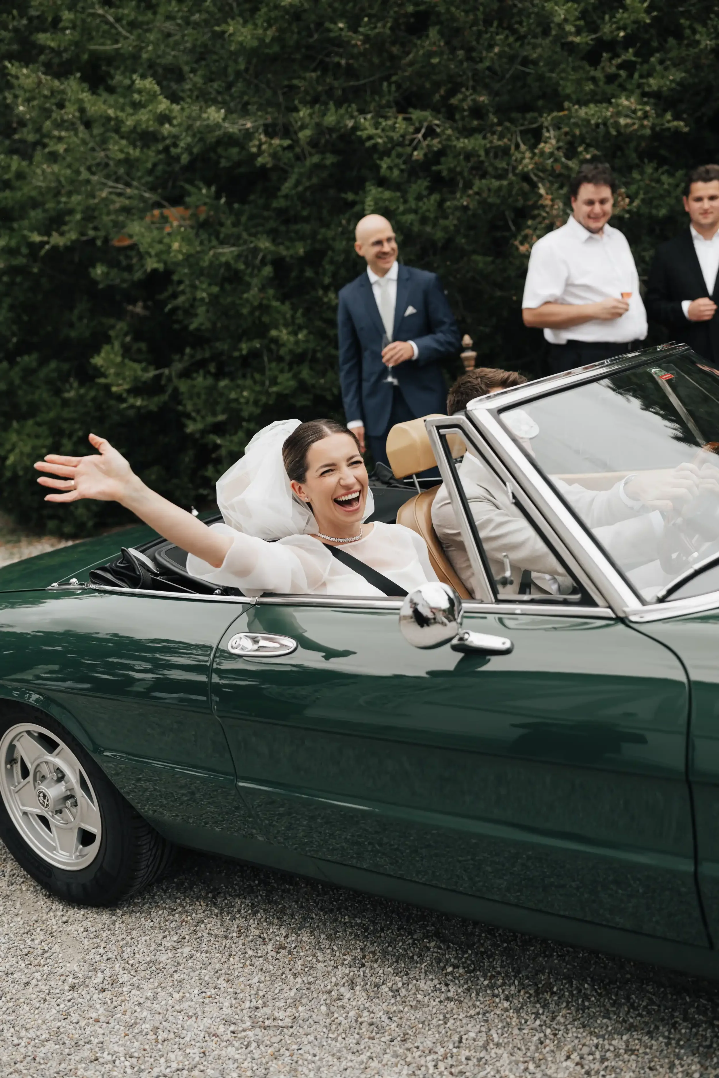 Bride and Groom in Green Vintage Car: Bride is laughing and waving