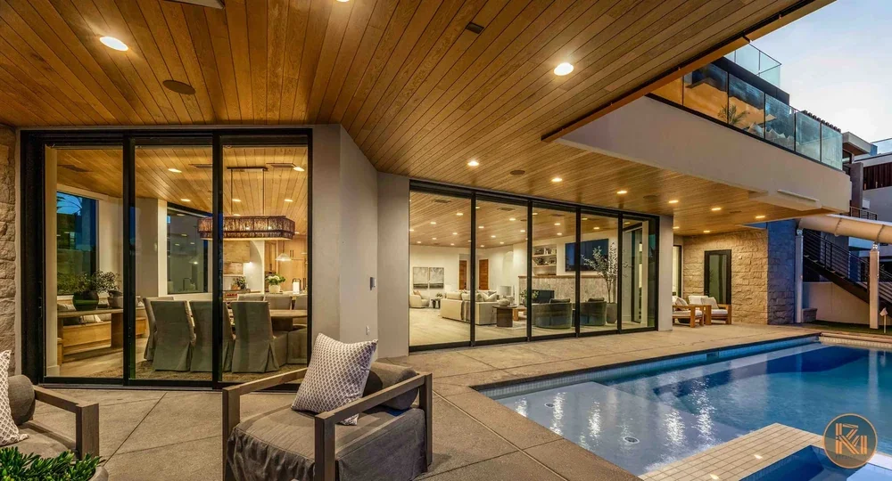 Modern home with illuminated glass walls, covered patio and swimming pool at dusk, photographed by Sam Reed.