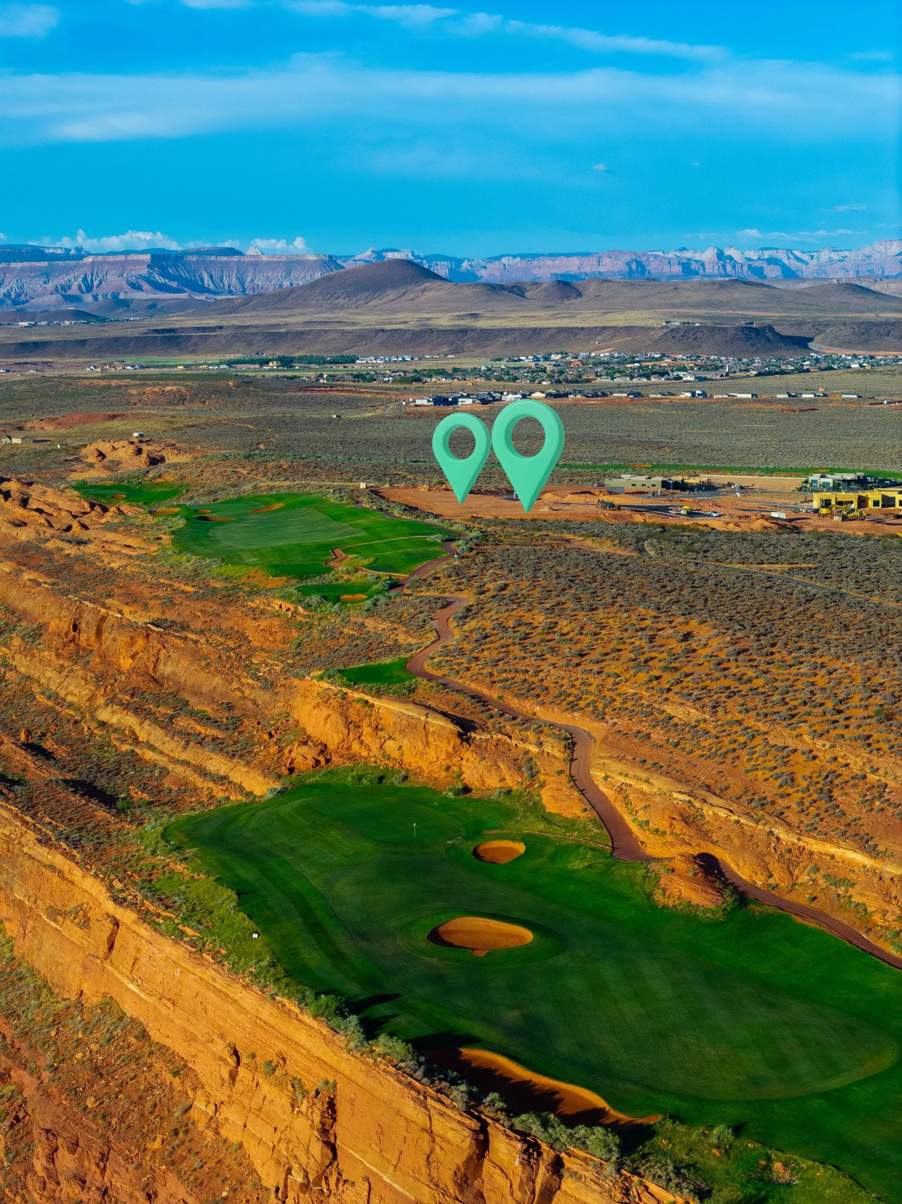 Aerial view of a Southern Utah golf course and desert cliffs, with two mint-colored property markers.