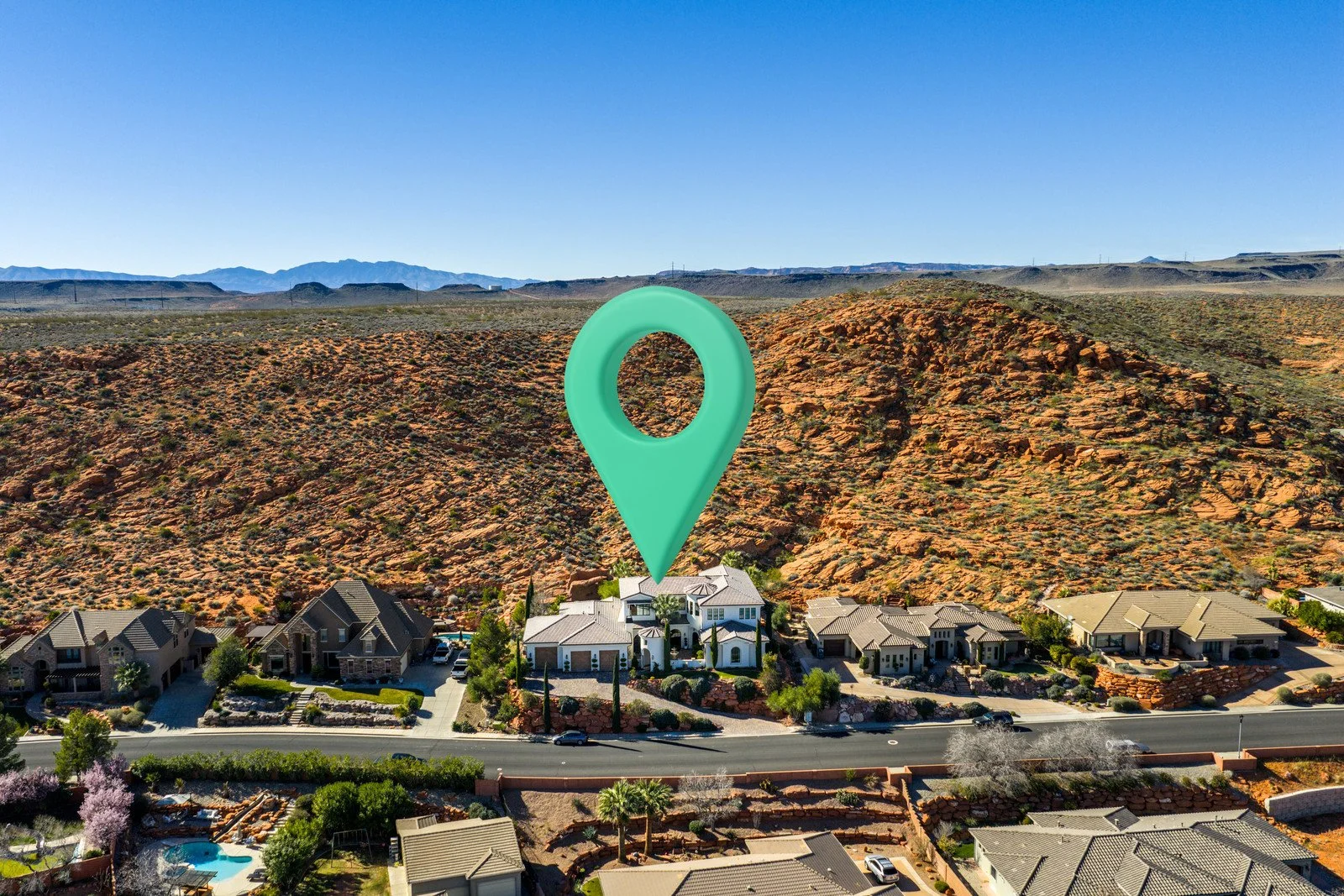 Aerial view of homes below red desert hills, with a mint-green location marker above the central white house