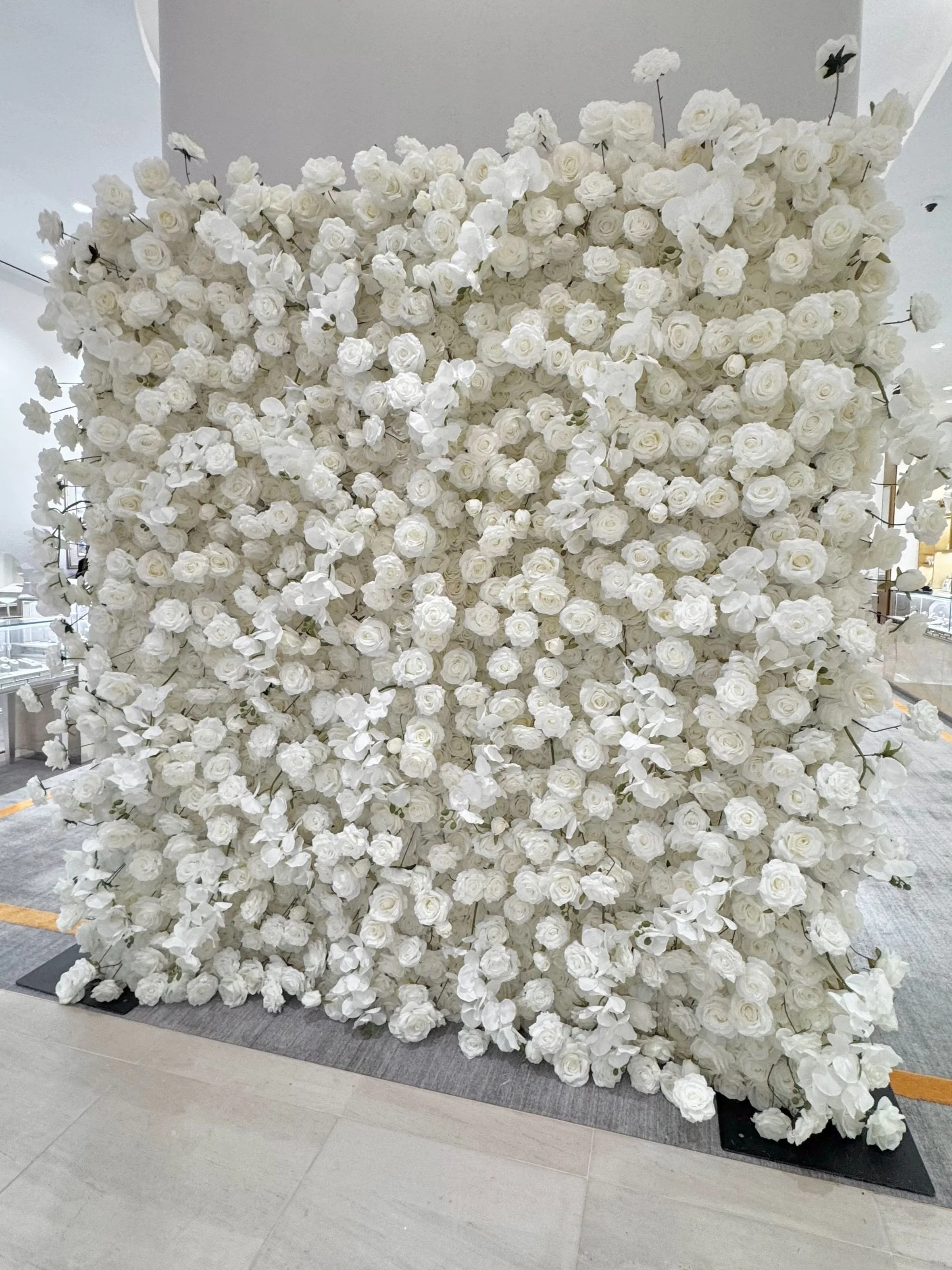 Large decorative display of white roses and orchids arranged in a square pattern in an indoor setting. white flower wall in short hills mall best for events rentals gorgeous