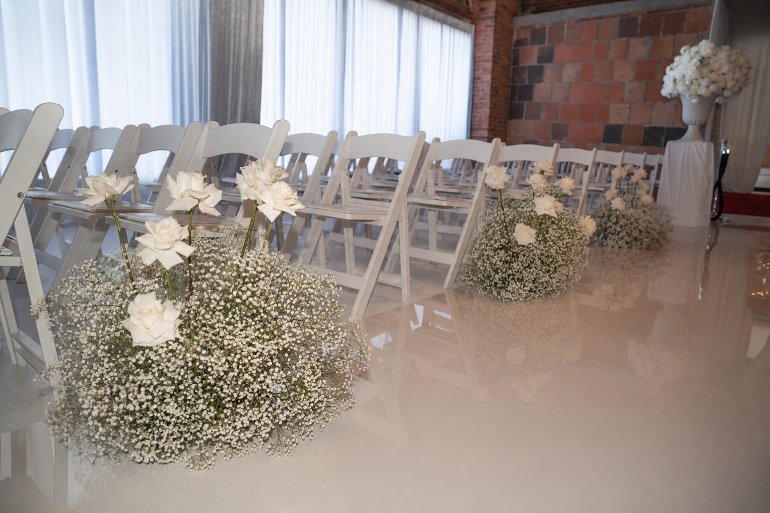 Wedding ceremony setup with white chairs and floral arrangements of white roses and baby's breath.