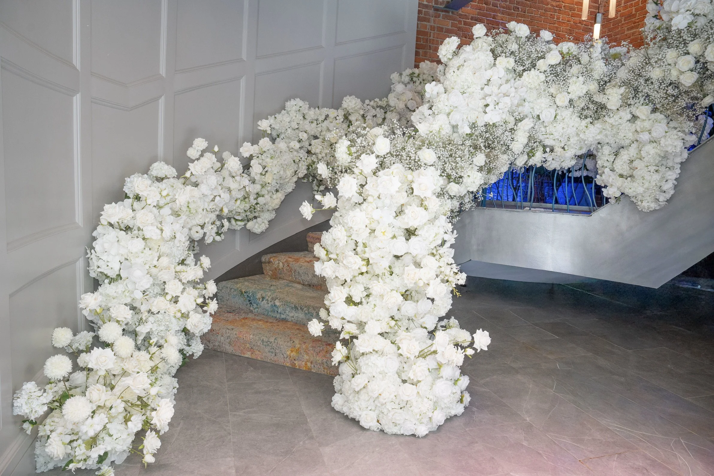 Wall decorated with an abundance of white flowers on a staircase with gray steps. stair wrapped with flowers for the Montclair mezzanine in NJ white 