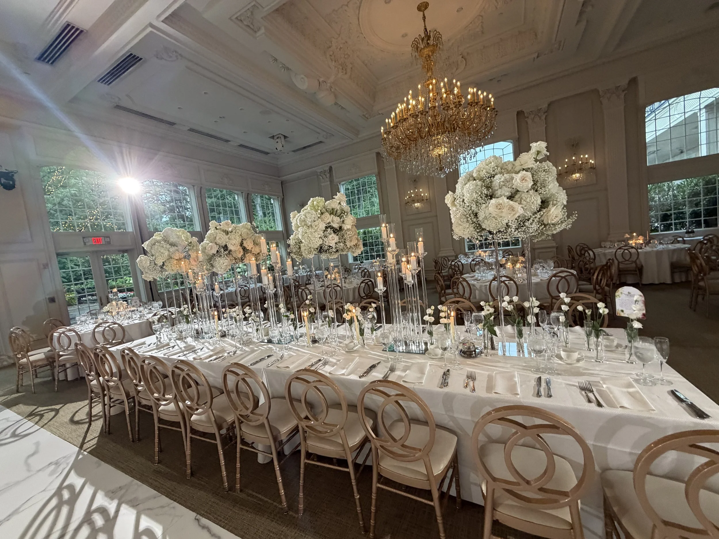White floral centerpieces under crystal chandeliers in a ballroom