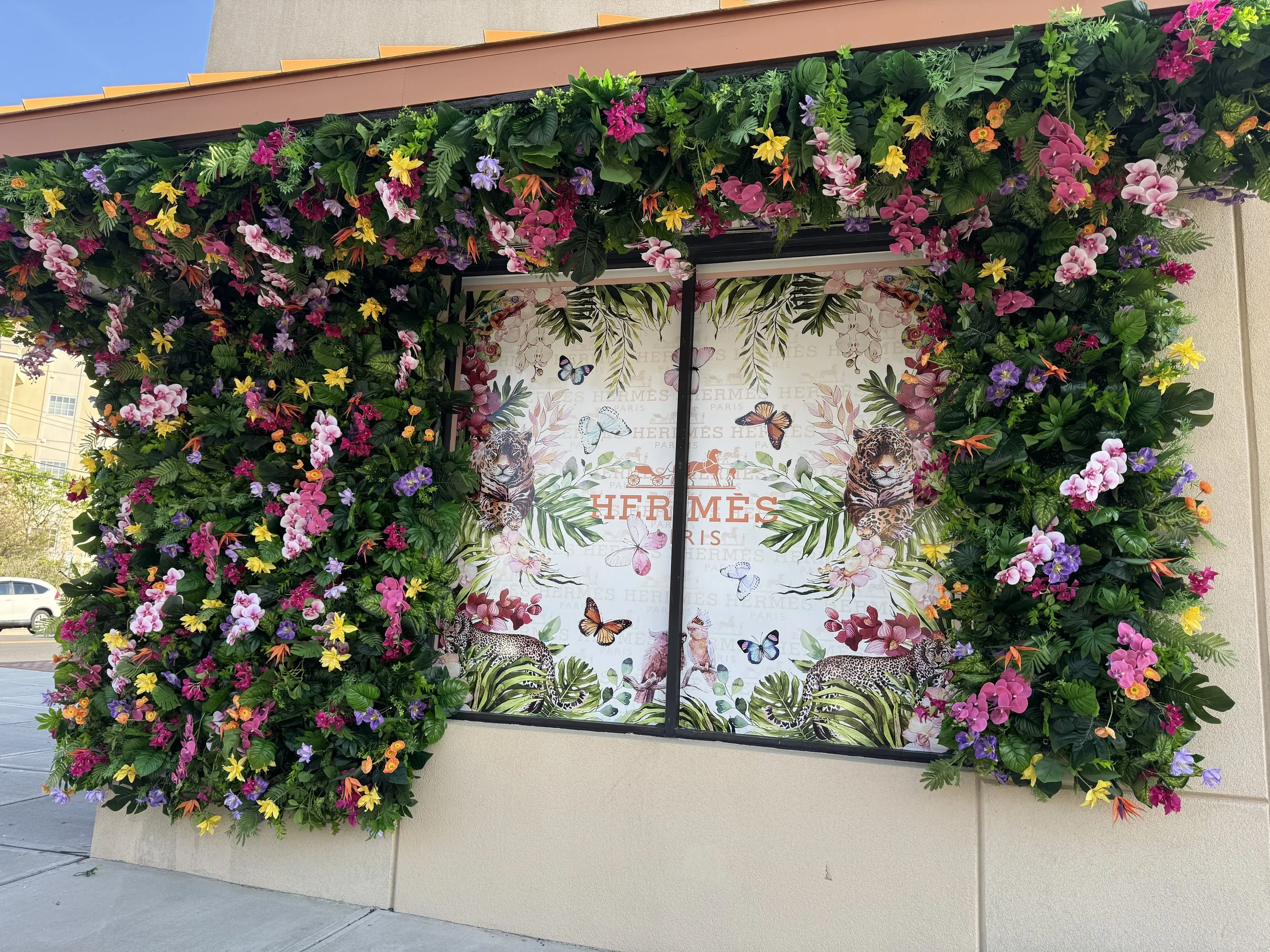 Storefront with lush flower arrangements and imagery of leopards, butterflies, and tropical plants, with Hermes branding in the background.