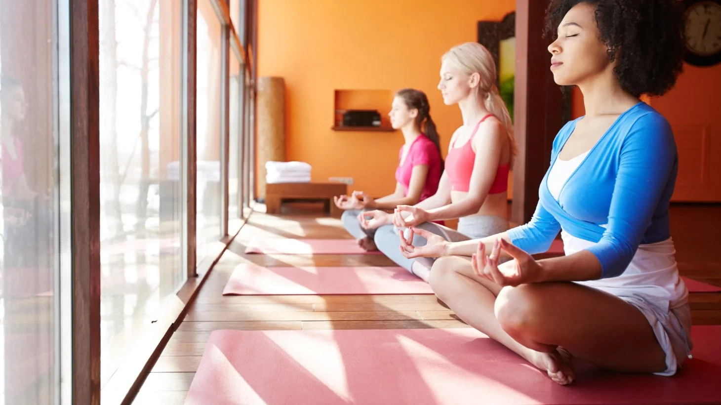 Three female yogis on pink mats, meditating.