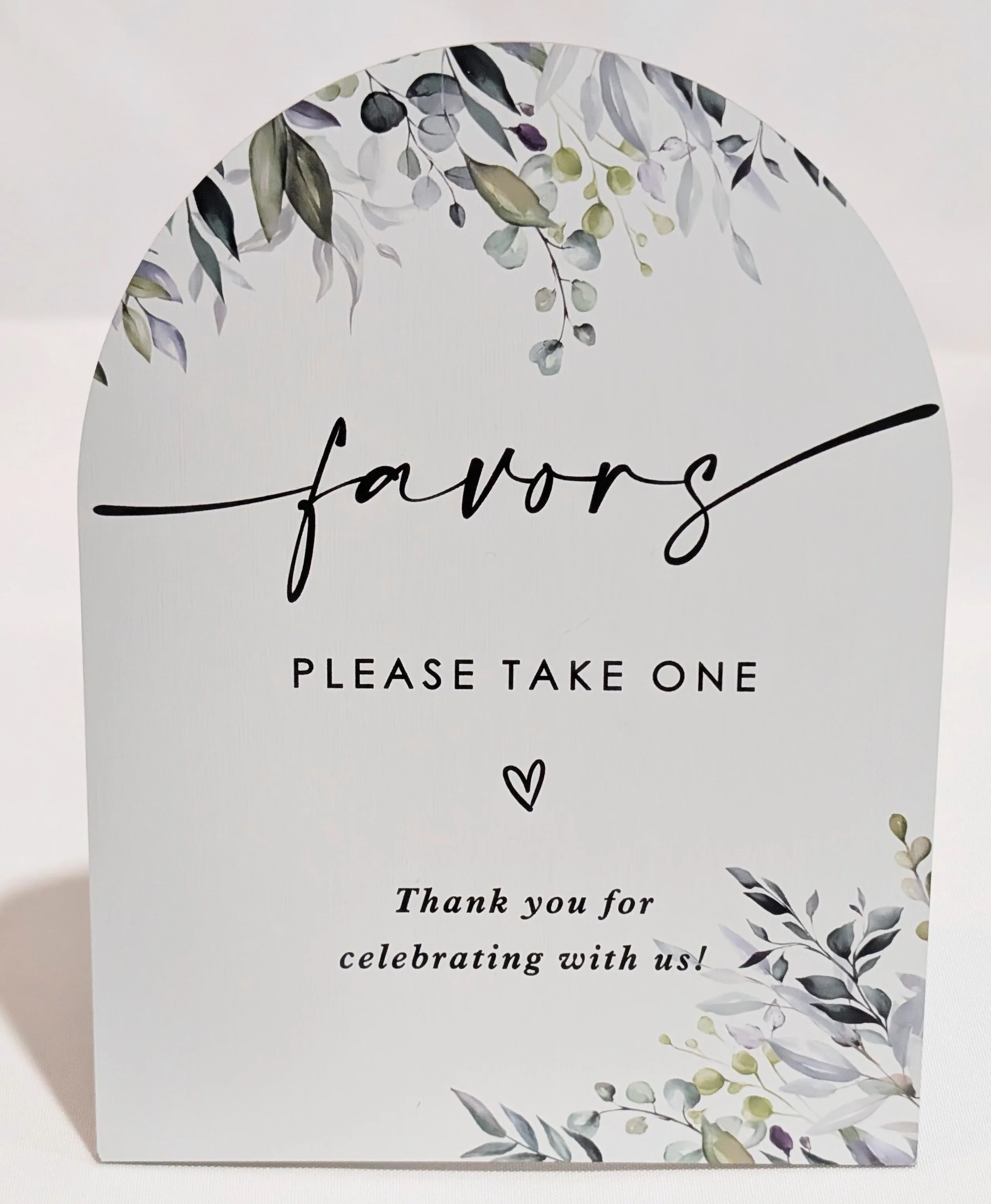 White arched sign with botanical accents "Favors. Please take one. Thank you for celebrating with us!"