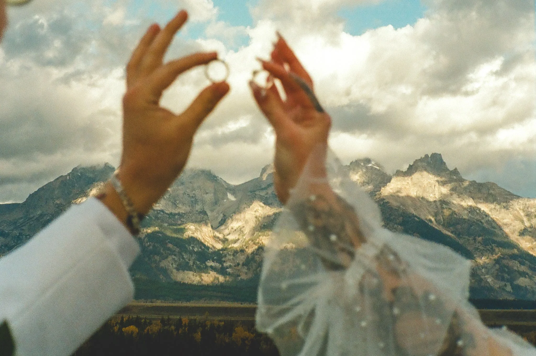 an elopement couple holding their rings up with the Tetons in the background