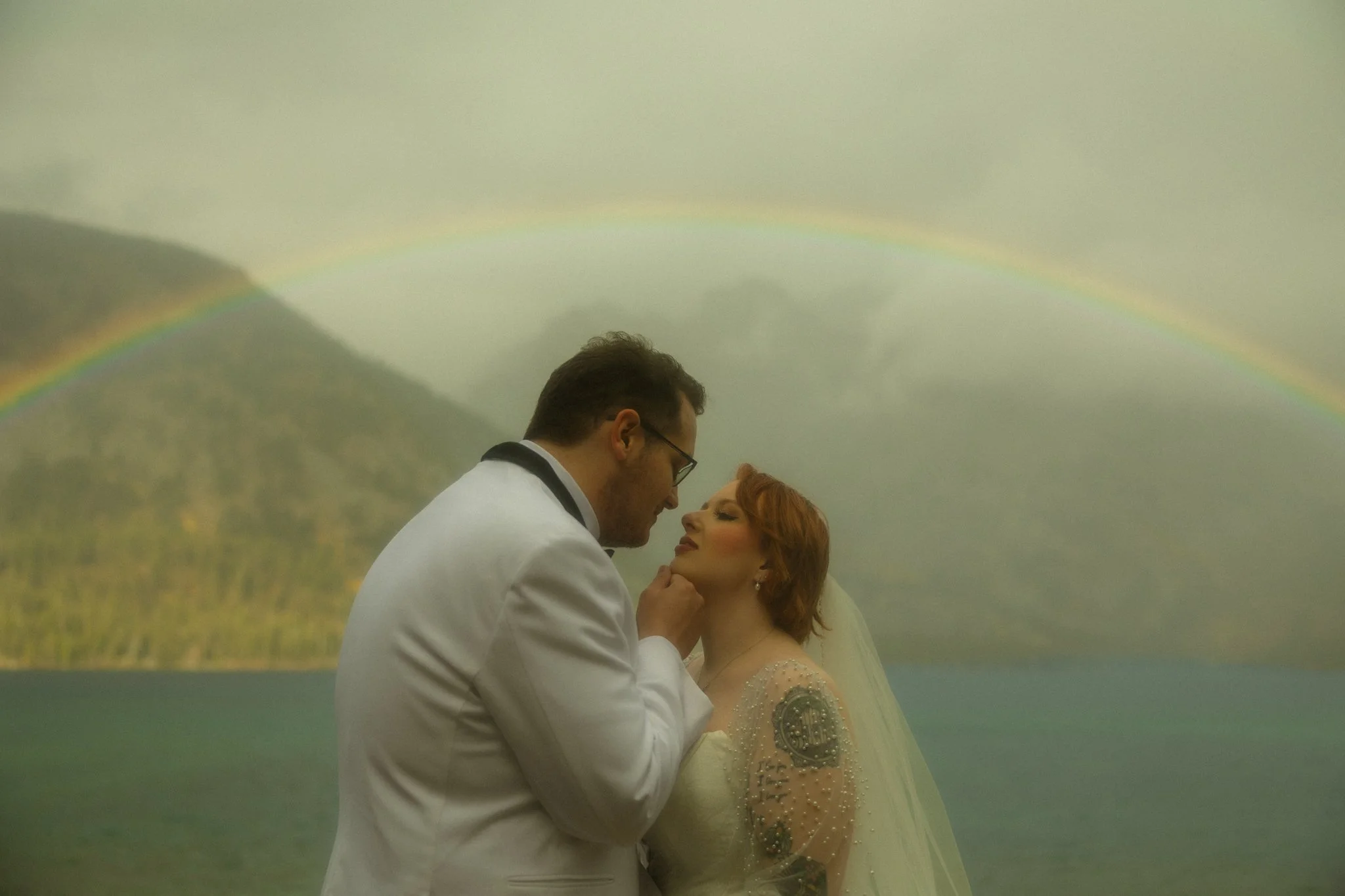 an elopement couple leaning in for a kiss under a rainbow in Grand Teton National Park