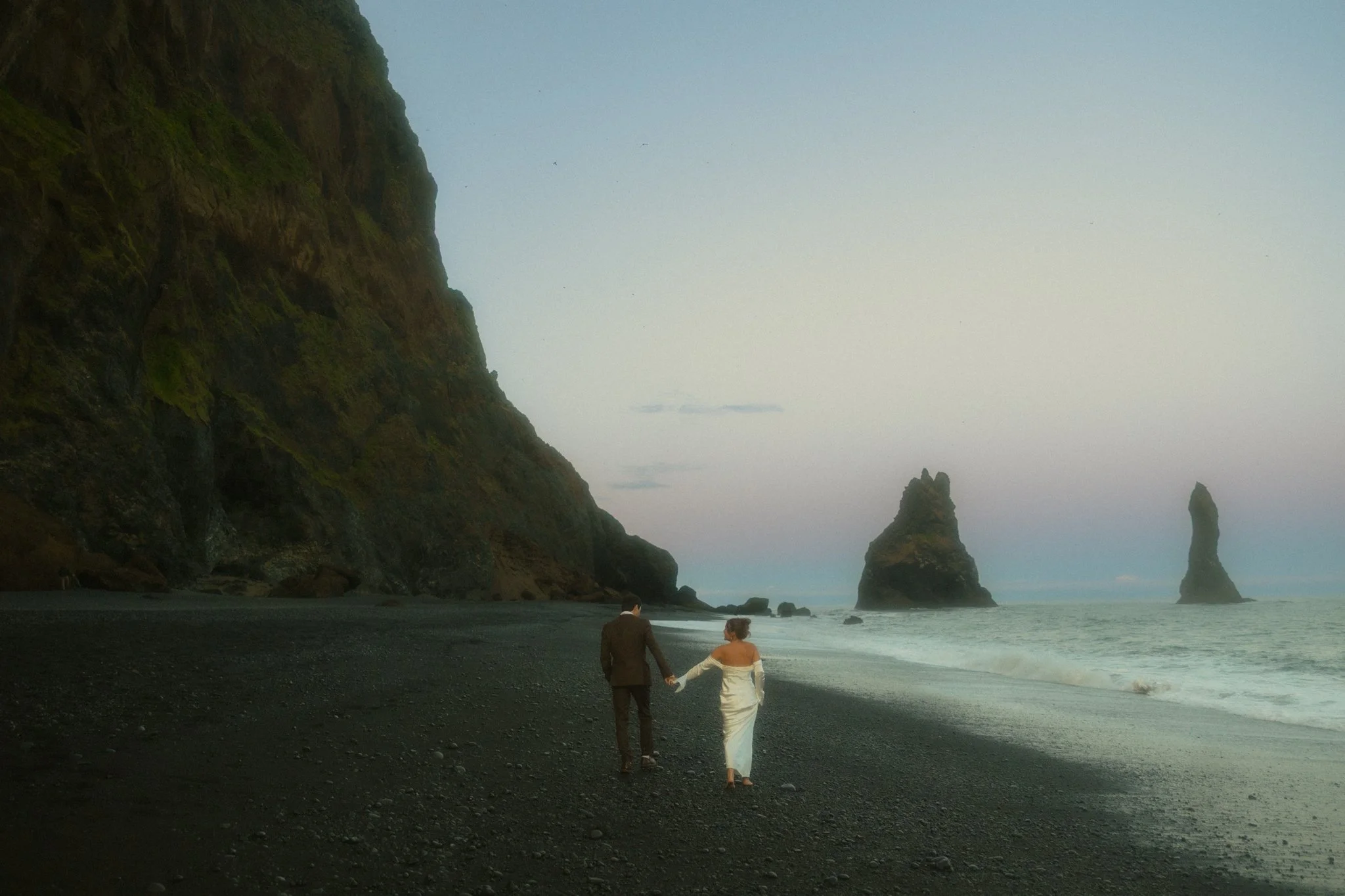 an elopement couple walking along the shore on an Iceland black sand beach