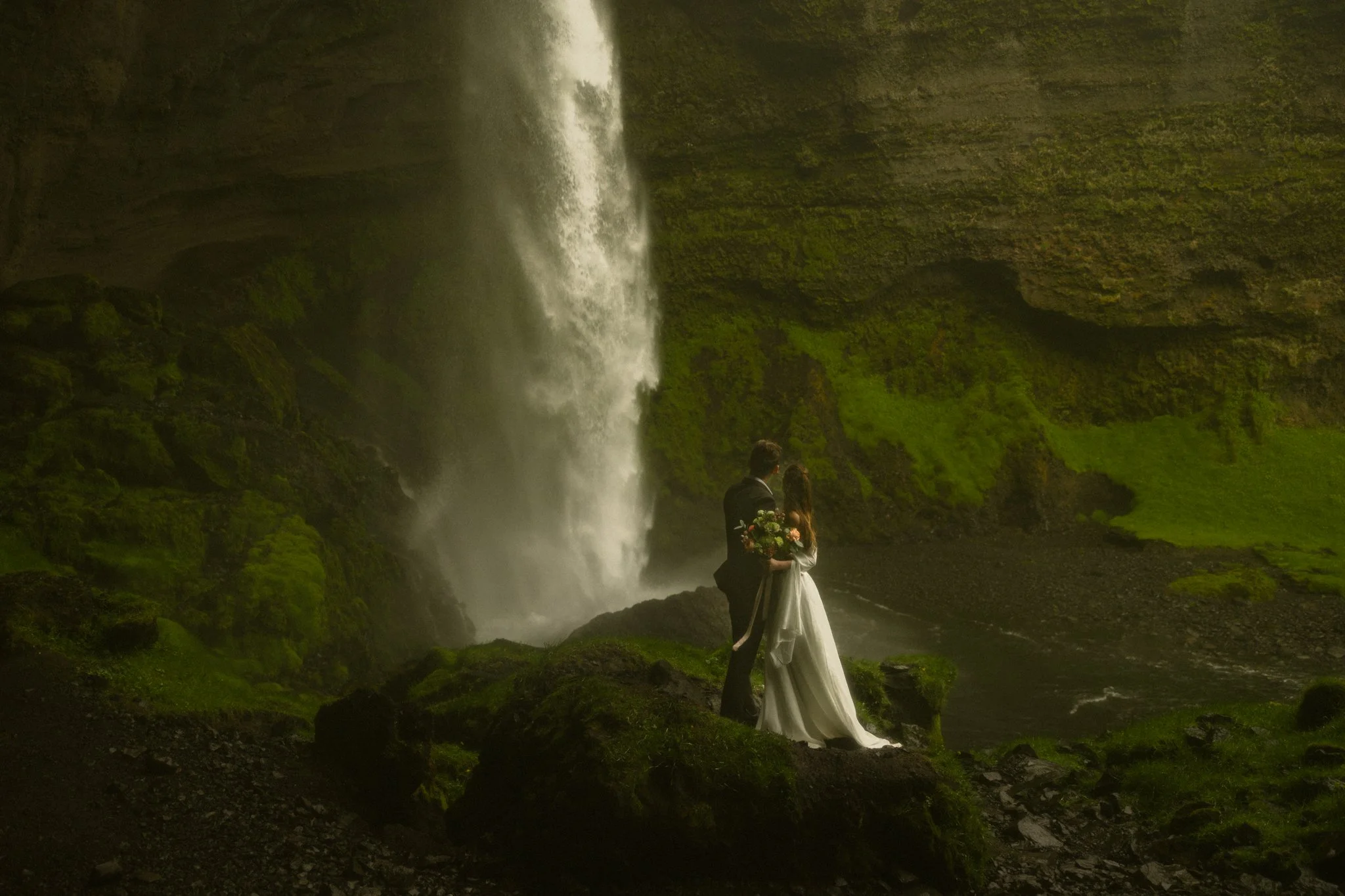 an elopement couple standing under a waterfall in Southern Iceland