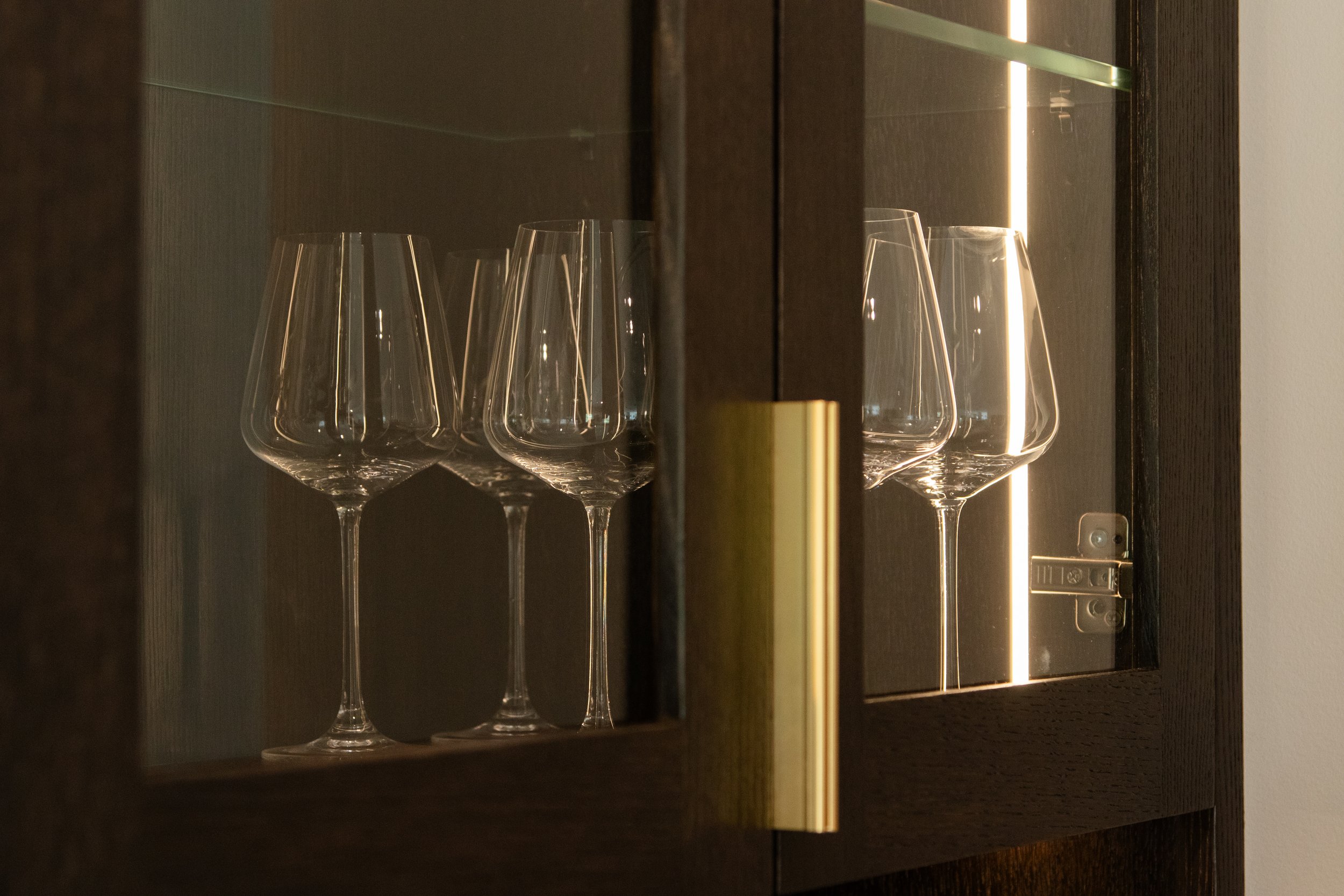 A luxury solid wood cabinet with a glass door, containing several empty wine glasses arranged in a row.