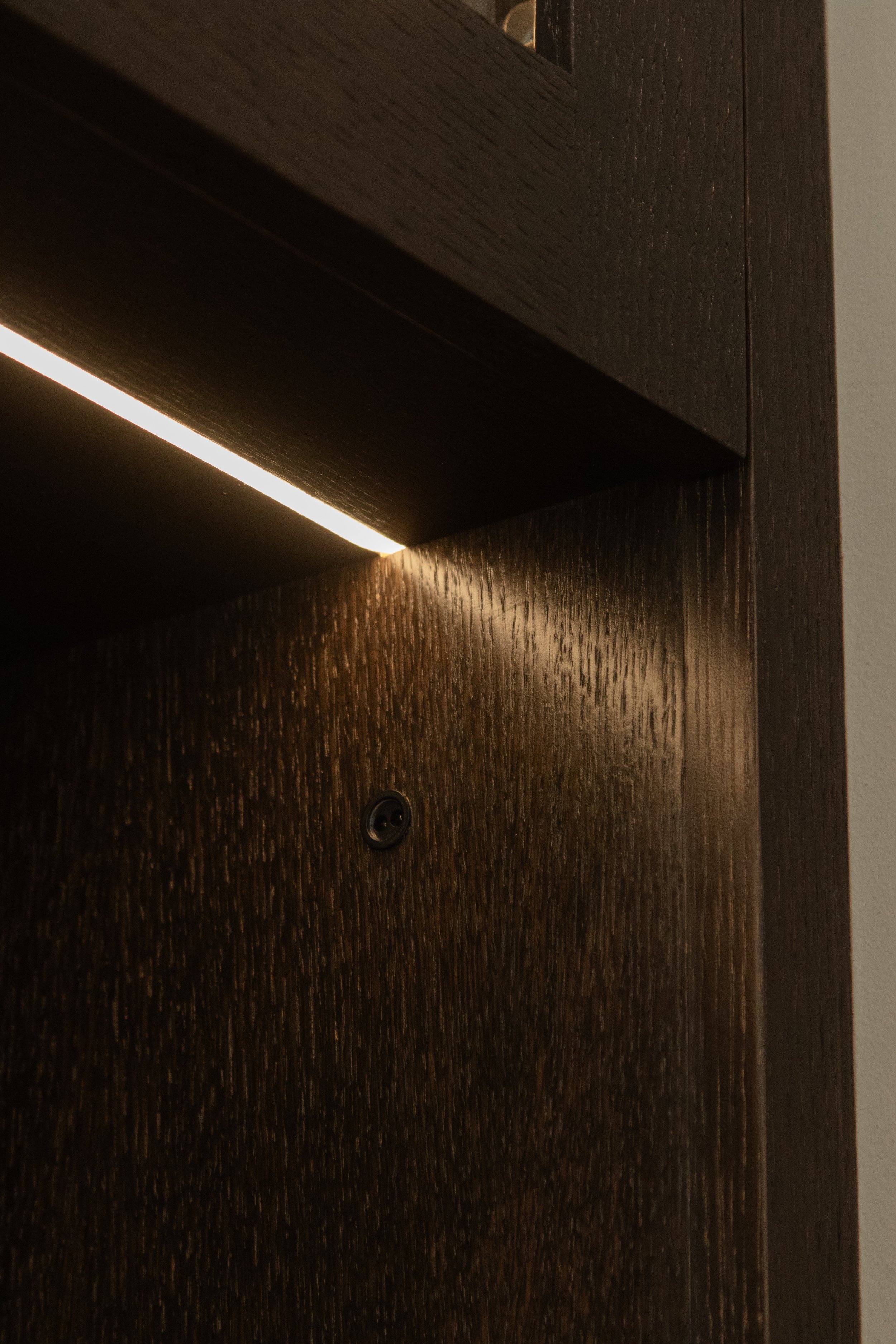 Close-up of a dark wooden door with a touch sensor and a narrow strip of light coming from underneath.
