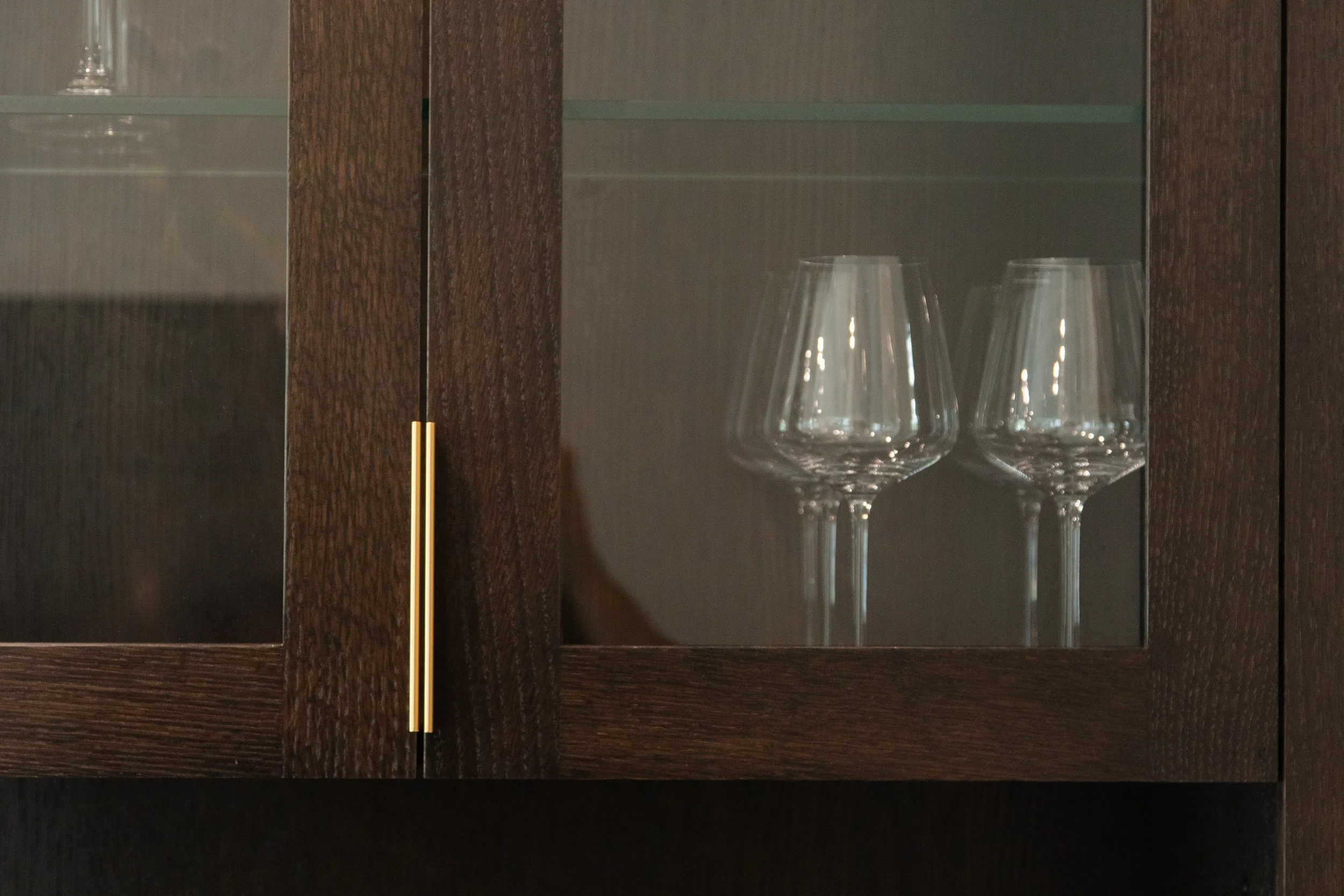 A dark wood cabinet with glass doors containing three empty wine glasses inside.