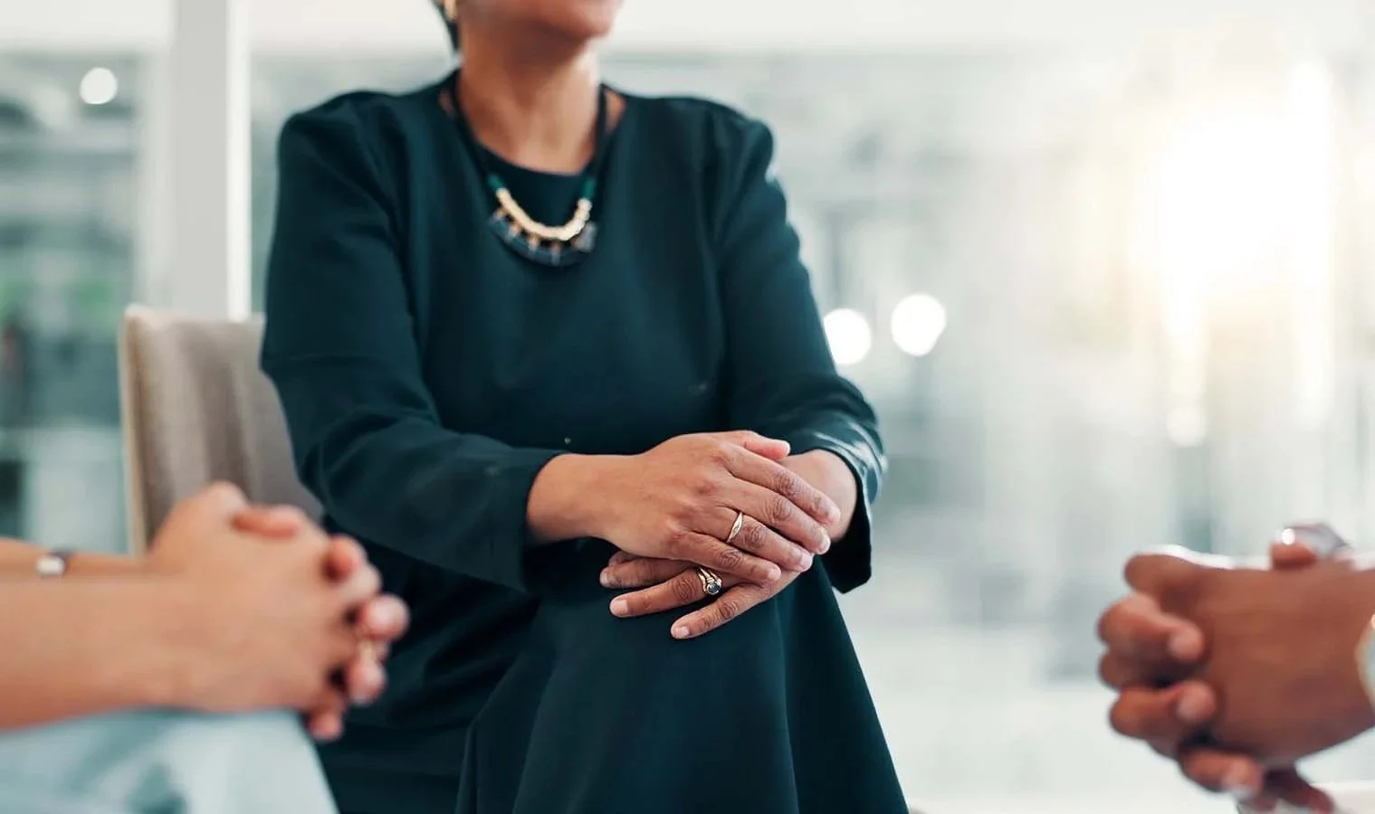Nonprofit HR specialist sitting with her hands on her knees listening to two employees talk about a conflict.
