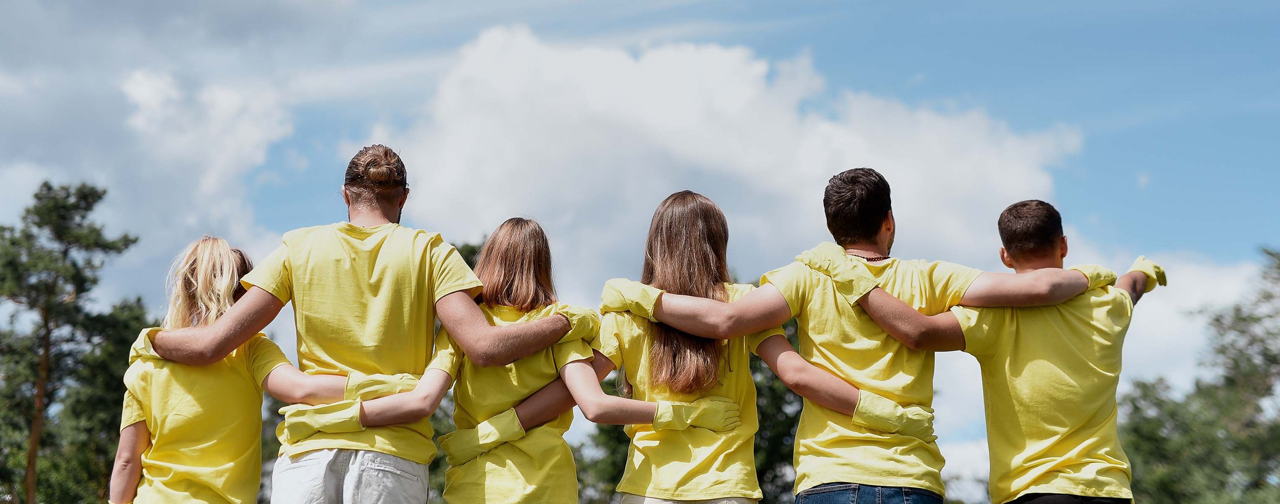 group of changemakers in yellow volunteer t-shirts standing together looking up at the blue sky