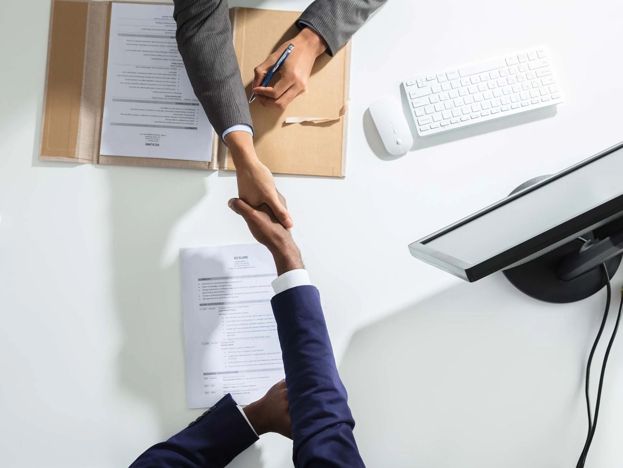 Nonprofit manager shaking the hand of a person interviewing while sitting at their desk with a printed resume in front of them.