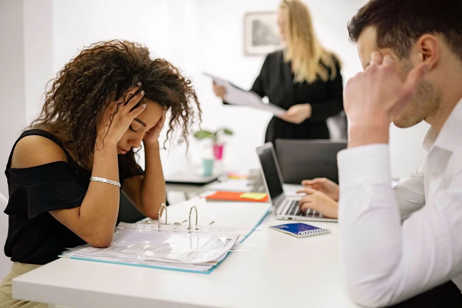 Coworkers working at office desk together while one stares hopelessly at information in a binder.
