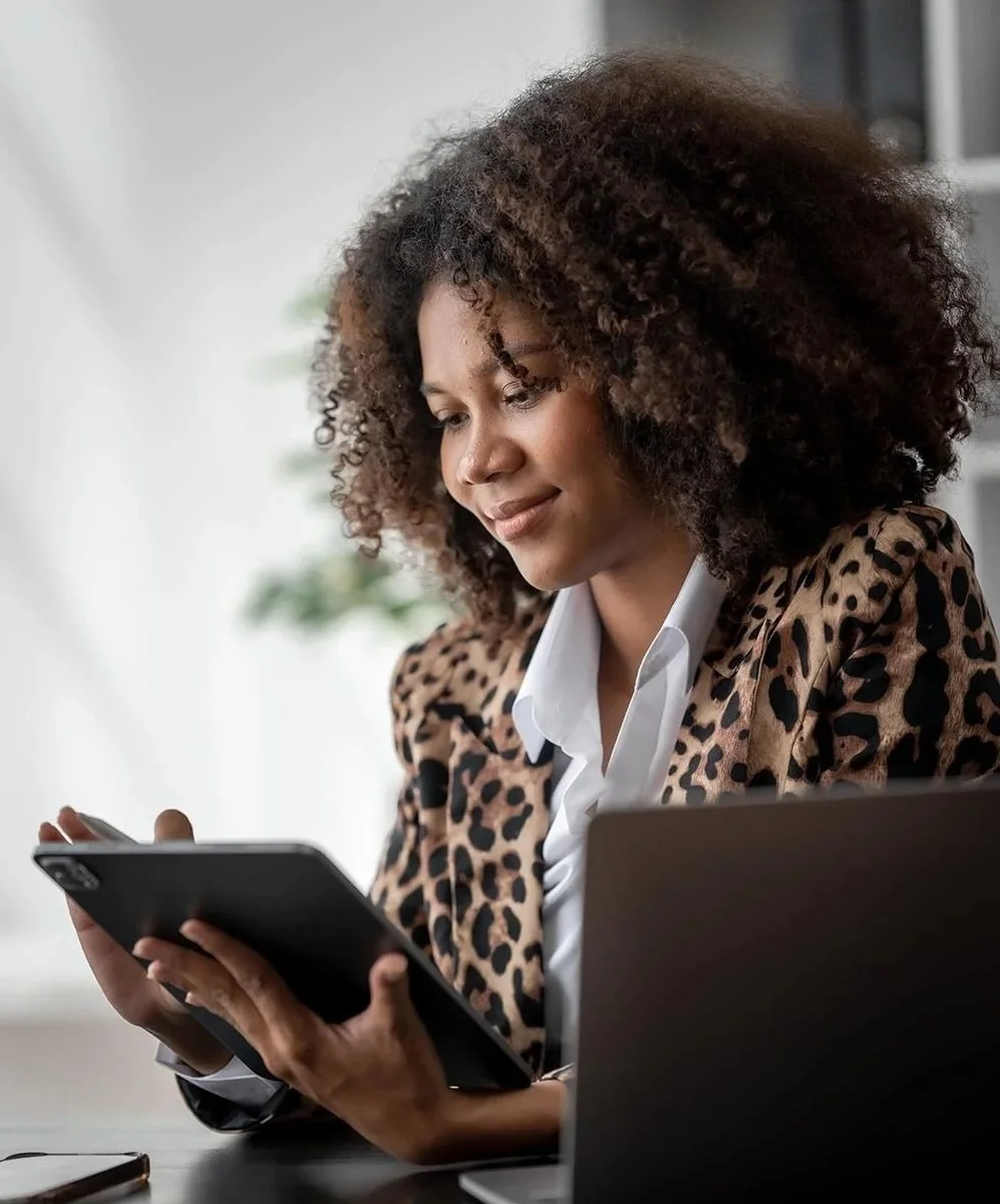accountant wearing a leopard print blazer carefully reviewing data on her tablet while seated at a desk with a laptop
