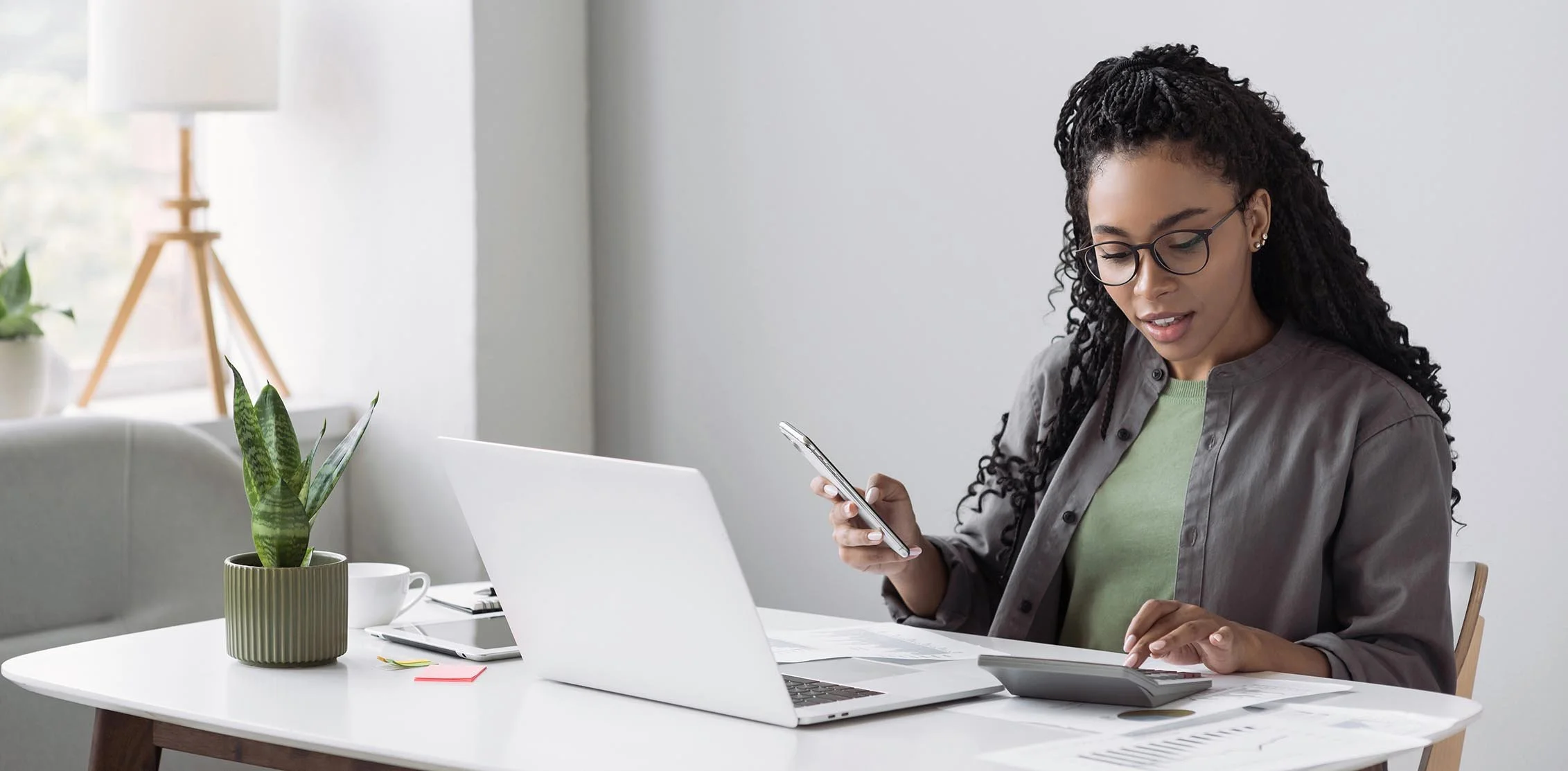 Woman sitting in front of laptop in a modern office working on nonprofit accounting using her calculator and phone.