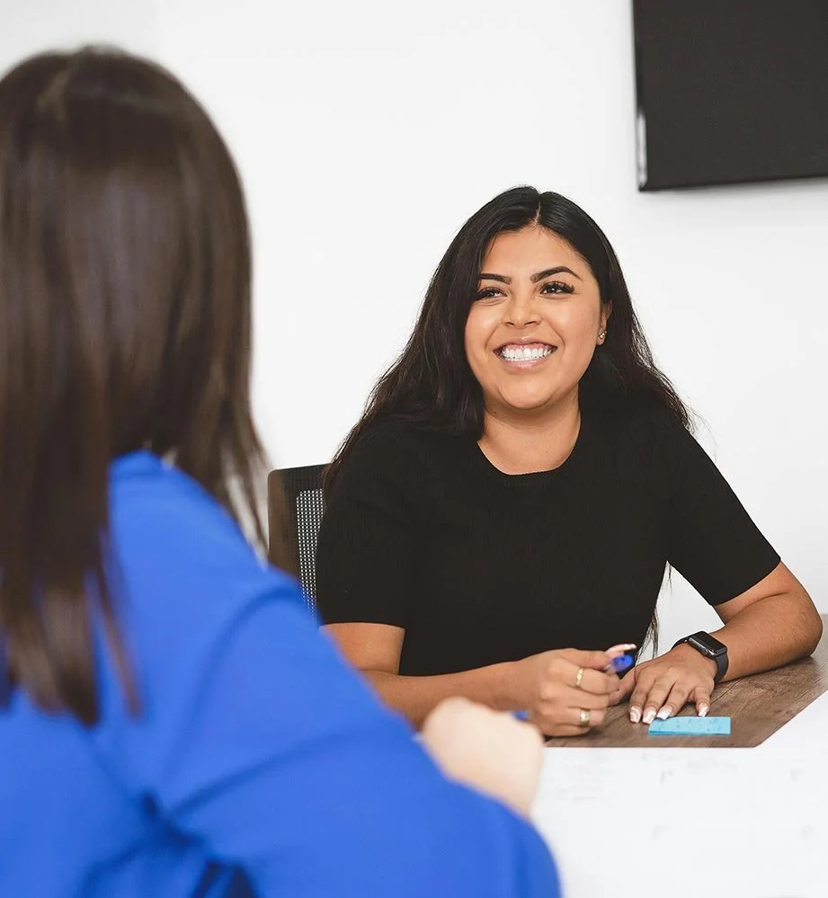 A young employee smiles and reviews performance documents with a manager during a positive performance management discussion