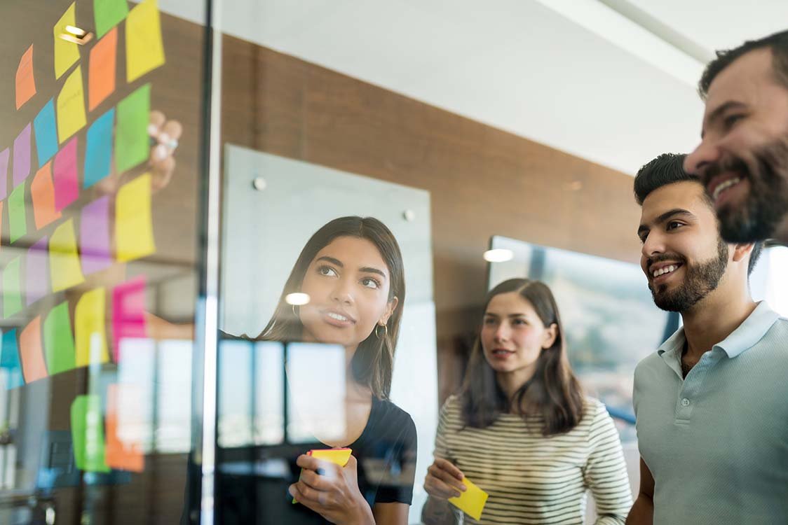 Team writing on post it notes stuck to an office window and discussing their strategy.