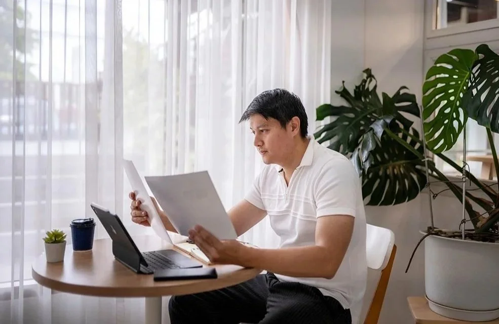 Man holding up two different printed reports and carefully comparing the financial information on them.