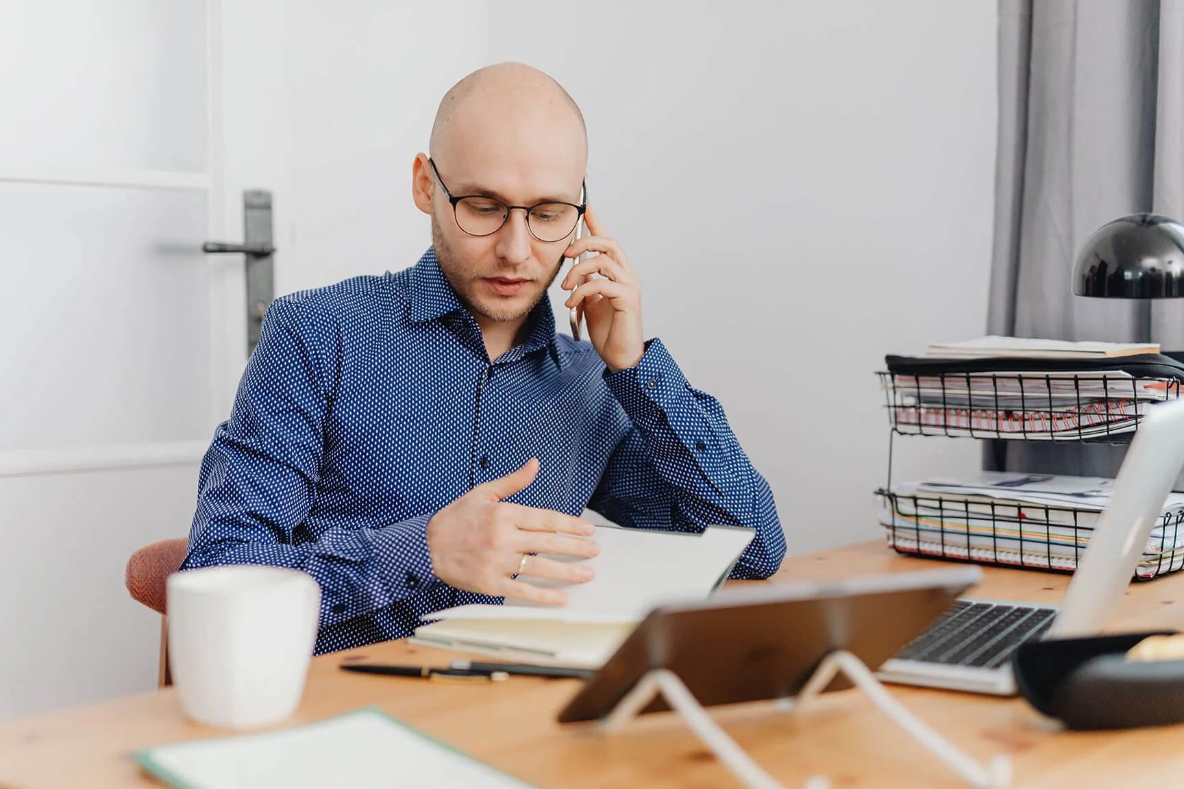 man sitting at desk talking on his cell phone while going through a notebook with his other hand