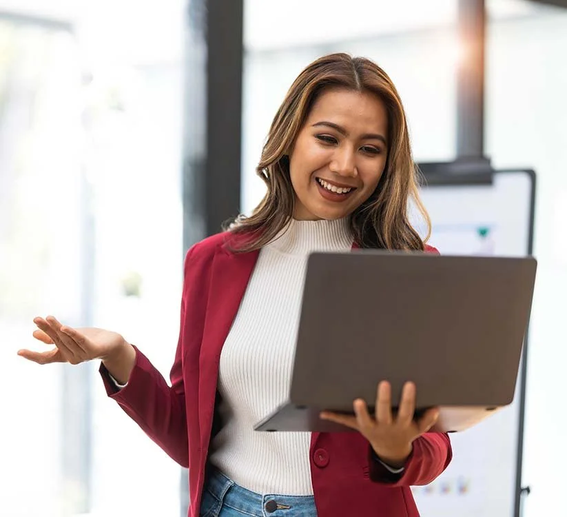 Woman standing and balancing her laptop in her hand while talking to someone on a video call.