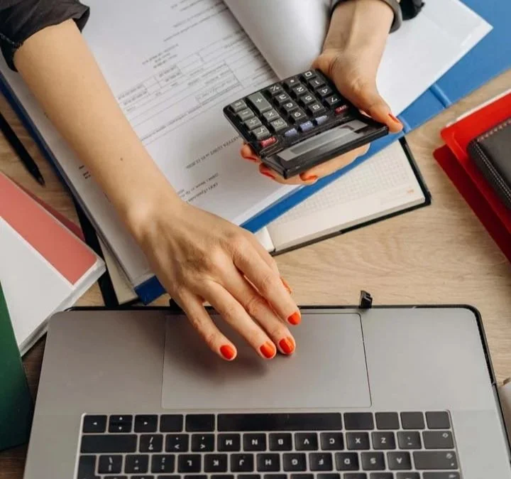 Woman doing accounting with calculator computer and lots of files.