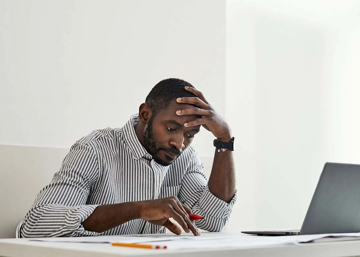 man looking concerned sitting at his desk using red pen to go through paperwork