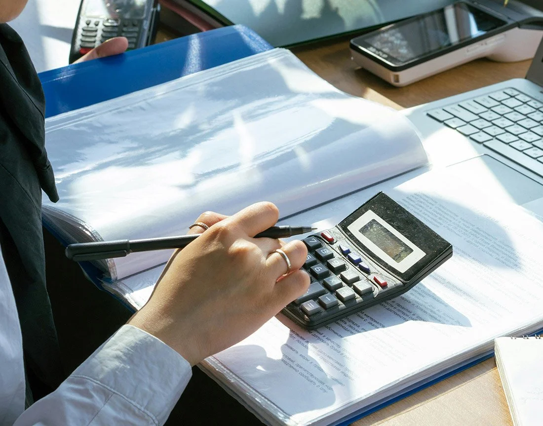 woman typing on calculator while reviewing the books and taking notes