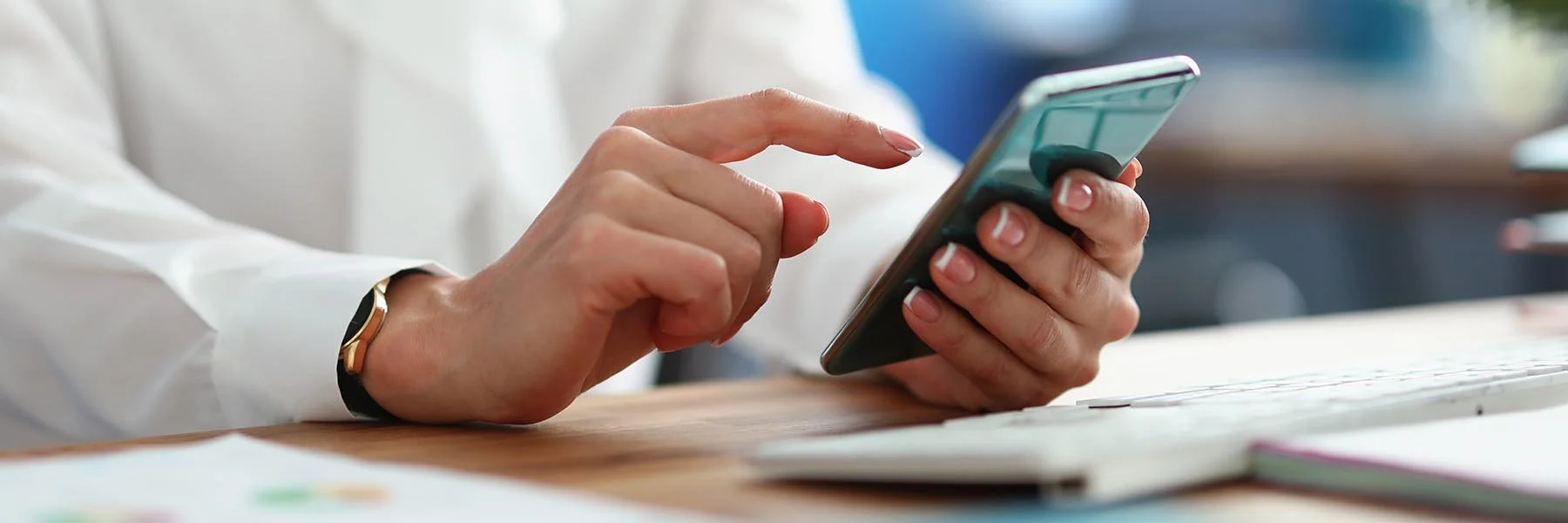 Woman in crisp white shirt using her cell phone while sitting at her computer.