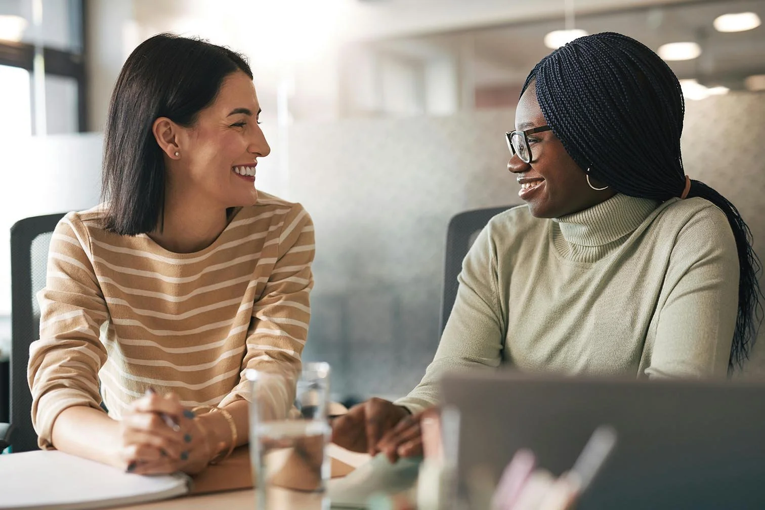 two nonprofit employees smiling warmly at each other while discussing project during meeting