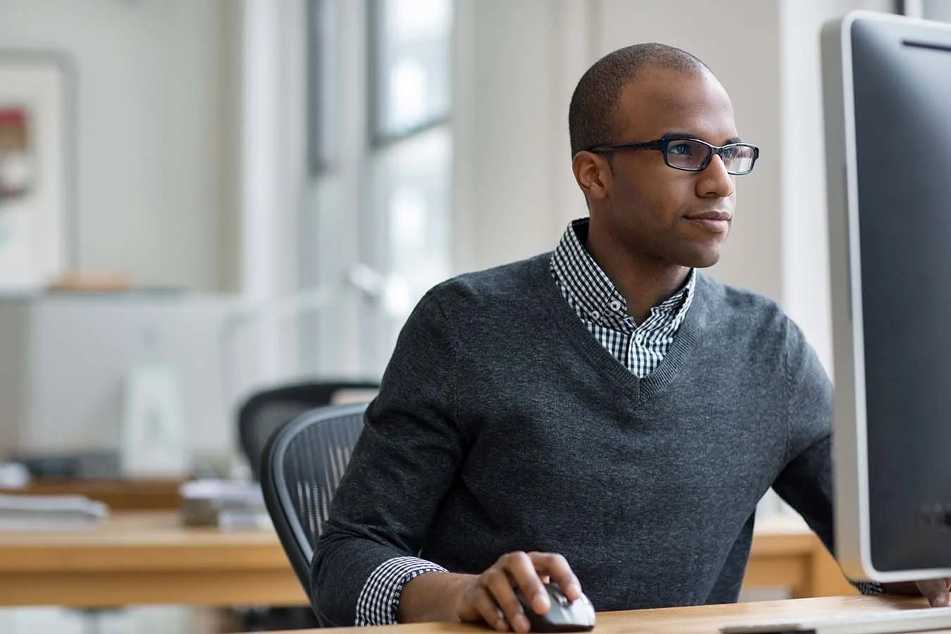 man in dark grey sweater and black glasses carefully reviews nonprofit accounting documentation on computer