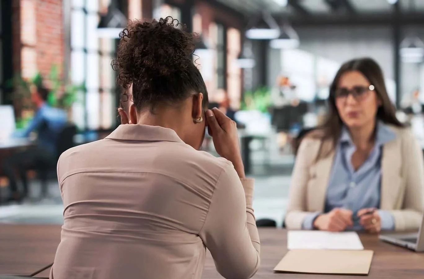 Frustrated woman holding her head and sitting at desk across from a nonprofit manager.