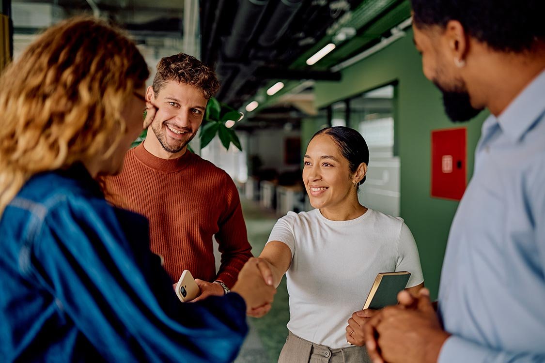 Fiscal sponsor team member meeting nonprofit team and shakes a woman's hand in a green office hallway.