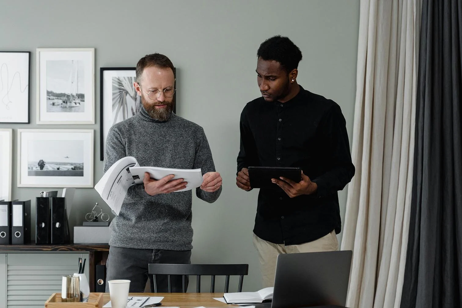 two men going over nonprofit accounting data with one holding a stack of papers while the other one cross references it with information on his tablet