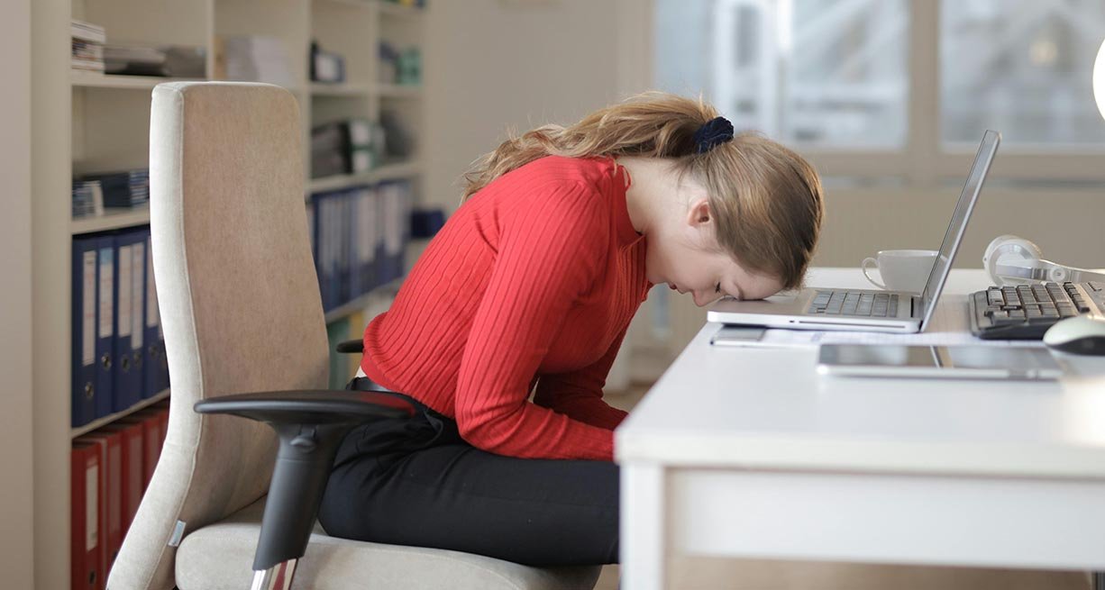 young woman at desk with her head on her laptop