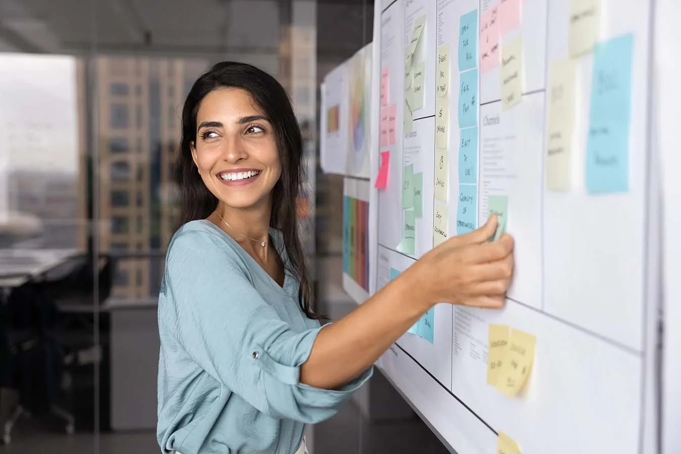 woman in blue blouse arranging sticky notes with writing on them on a board outlining their nonprofit strategy