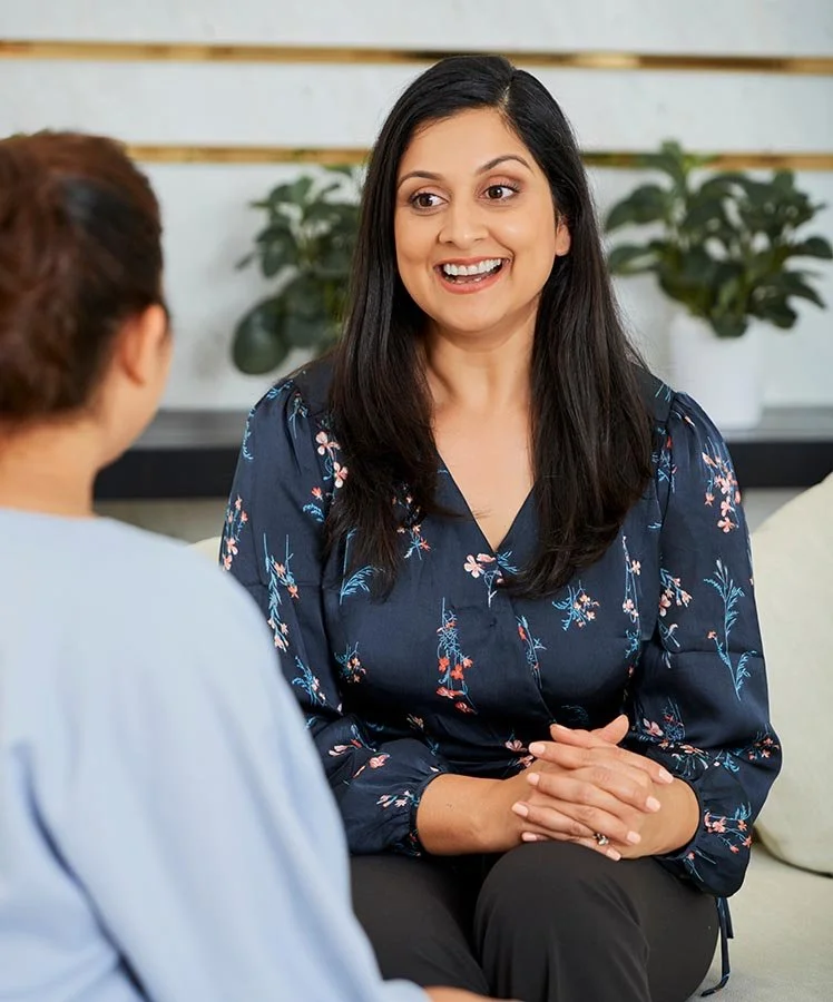 Fractional HR professional in flower blouse talking to nonprofit employee in office with plants behind them