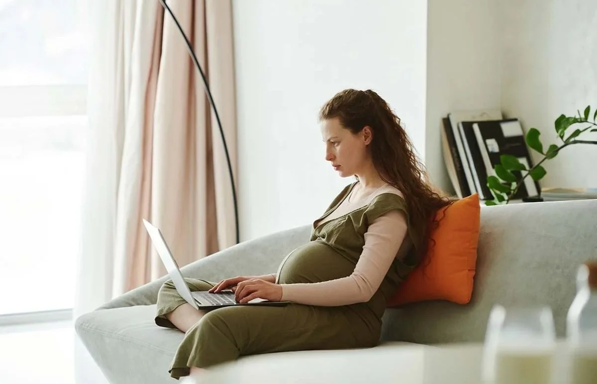 Pregnant woman sitting on a couch working intently on her computer.