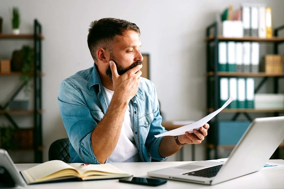 Man thoughtfully reviewing paperwork in his office.