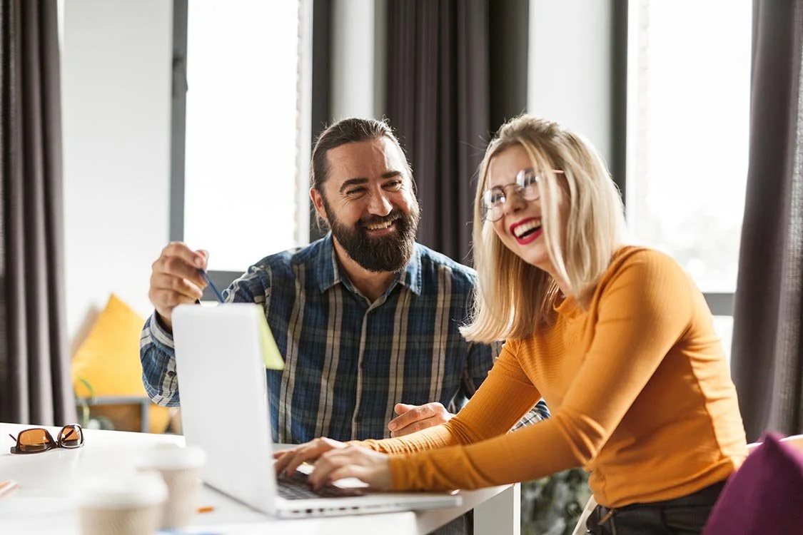 Nonprofit team member laughing while being trained by manager pointing to their computer screen as they type.