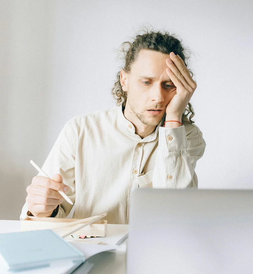 nonprofit team member sitting at desk in front of laptop taking notes during meeting and looking exhausted and overwhelmed